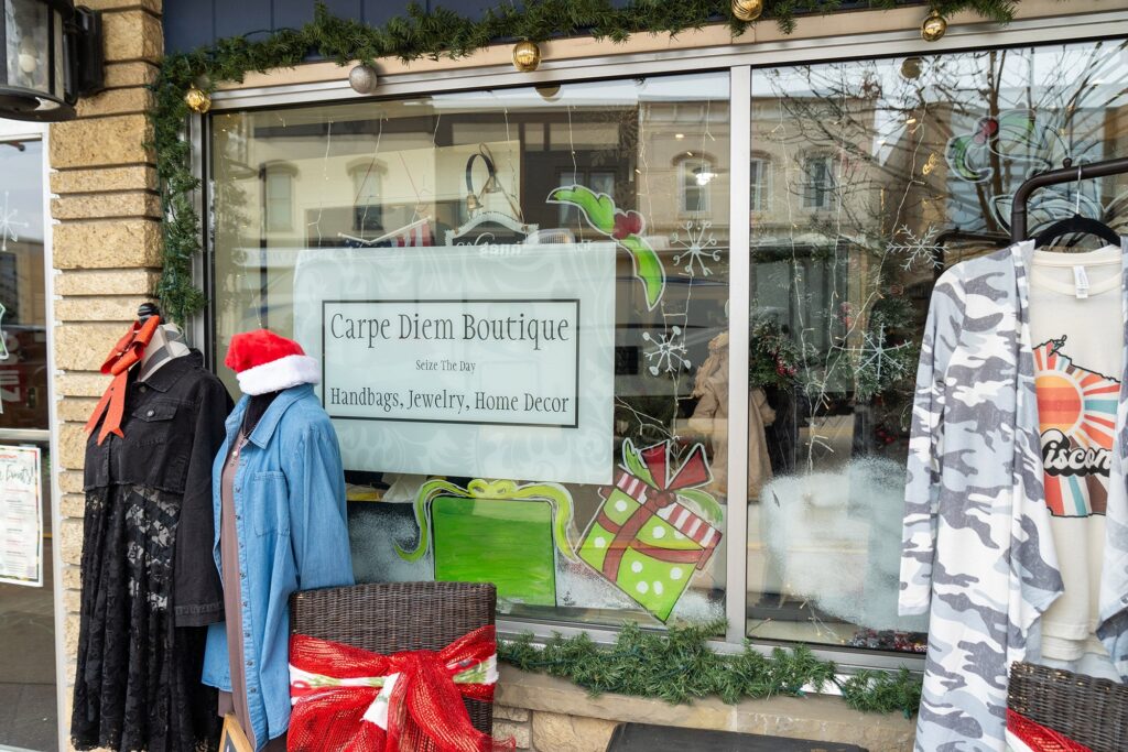 Storefront of Carpe Diem Boutique decorated for Christmas with mannequins displaying clothing. The window sign advertises handbags, jewelry, and home decor.