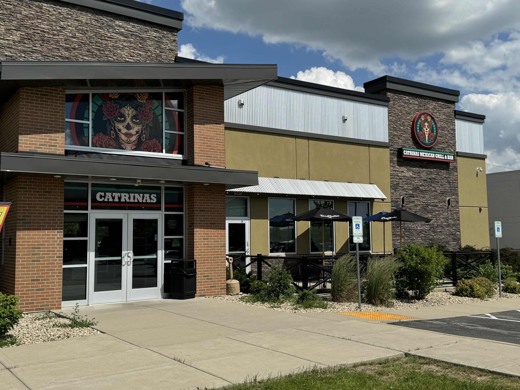 Exterior of a restaurant named "Catrinas" with brick and siding facade, colorful artwork above the entrance, and outdoor patio seating.