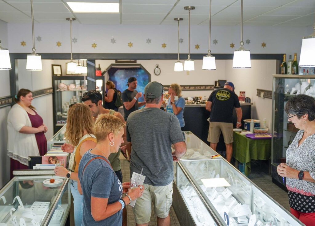 People browsing and shopping in a jewelry store with well-lit glass display cases and various items on display.