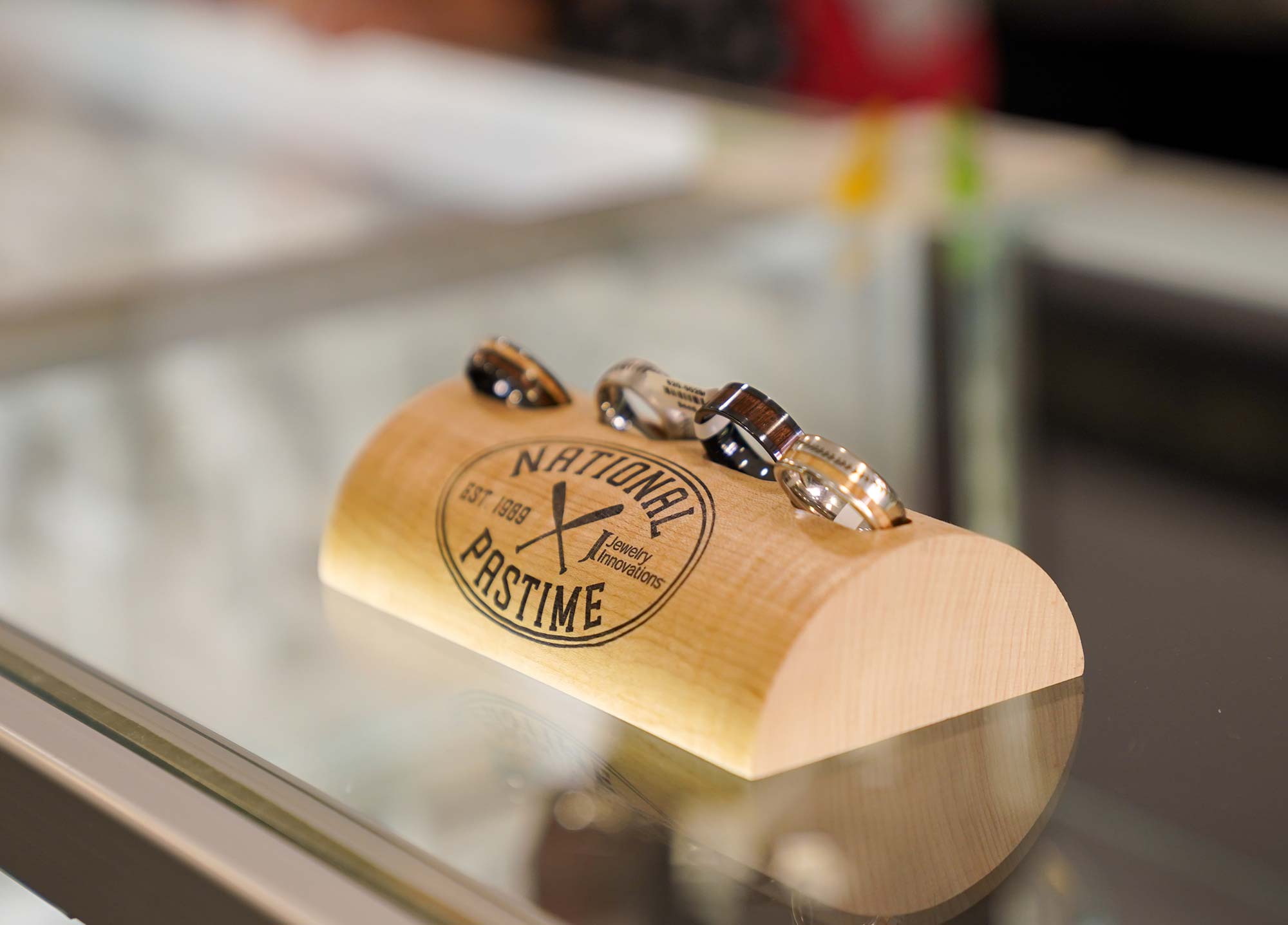 Three wristwatches are displayed on a wooden stand with the text "National Pastime" and "Est 1958." The stand is placed on a glass surface in a well-lit area.