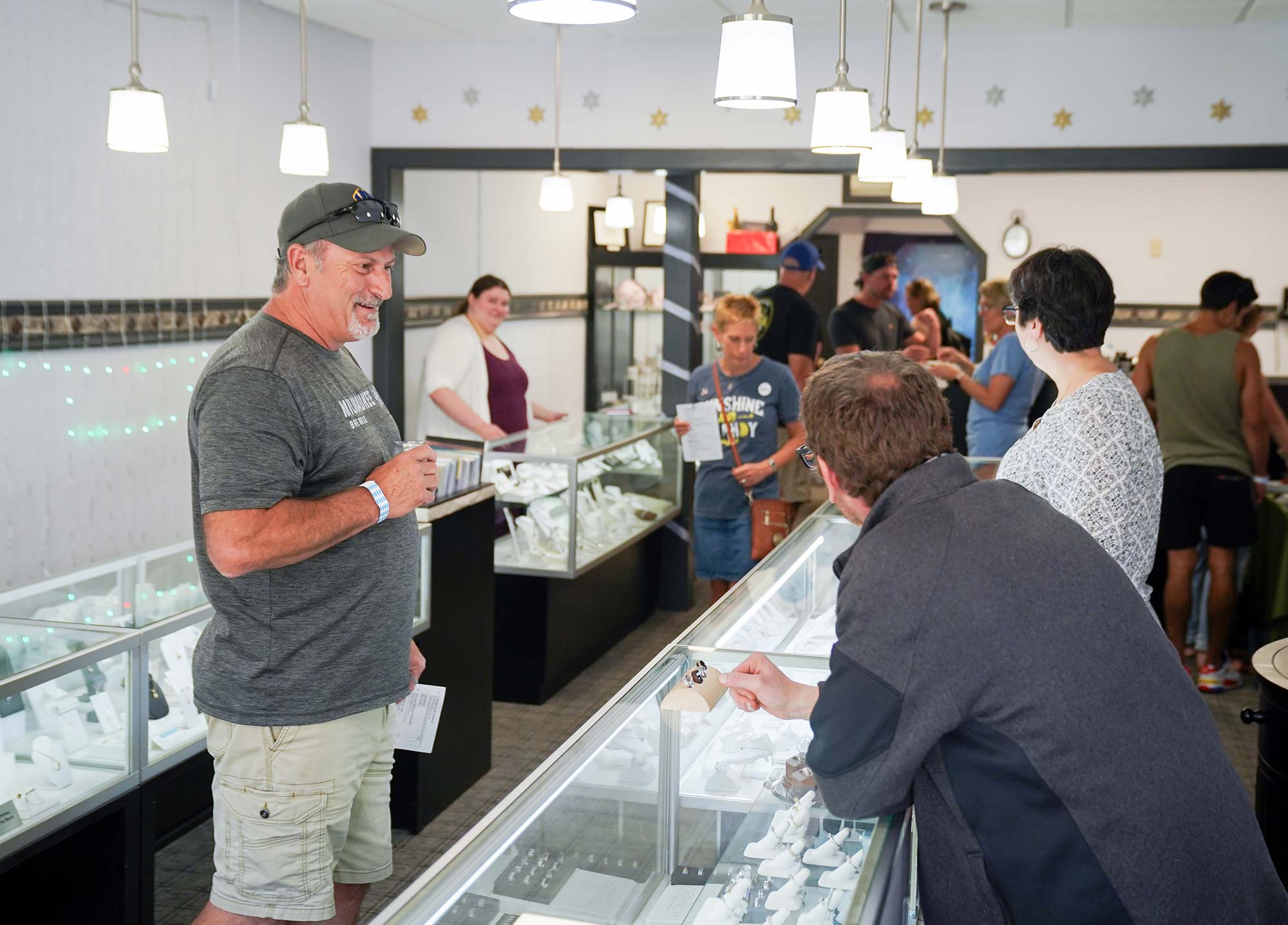 People inside a jewelry store looking at displays of rings and other jewelry items. Some individuals are talking to store staff.