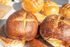 Close-up of assorted loaves of bread with varying crust patterns displayed on a table, with a prominent loaf featuring a cross cut on top in the foreground.