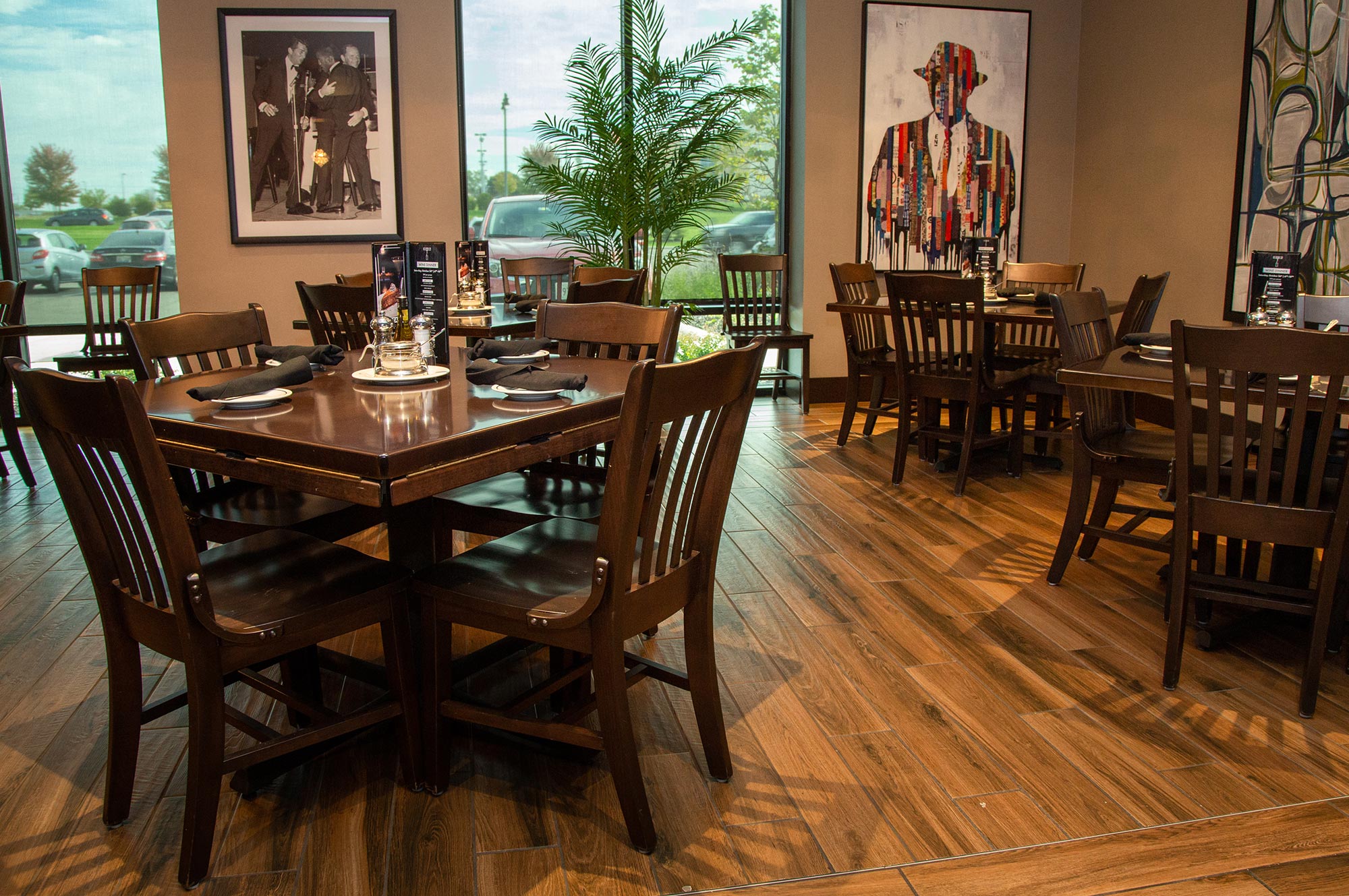 A modern restaurant dining area with wooden tables and chairs, contemporary artwork on the walls, and large windows providing natural light.