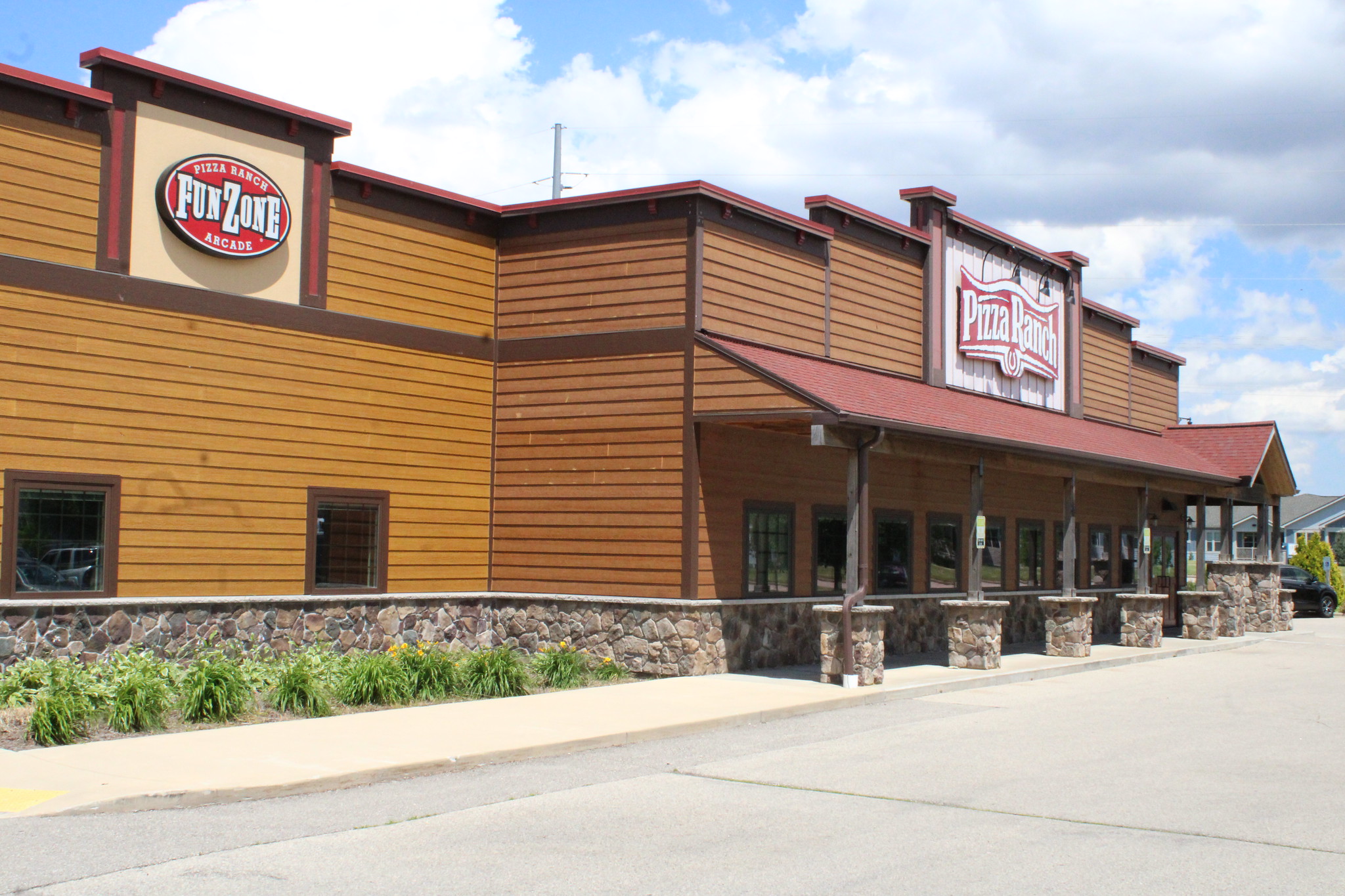 A large wood-paneled building with signs reading "Pizza Ranch" and "FunZone Arcade" on the exterior, under a partly cloudy sky.