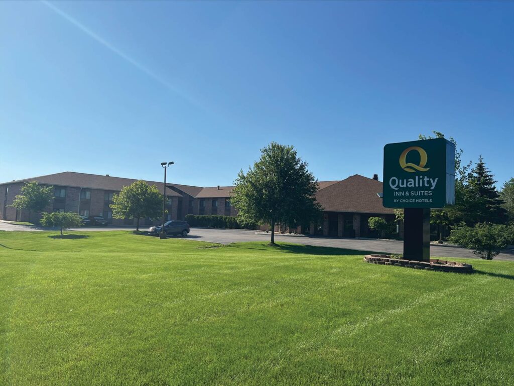 Quality Inn & Suites hotel with a large green lawn and a clear blue sky in the background.