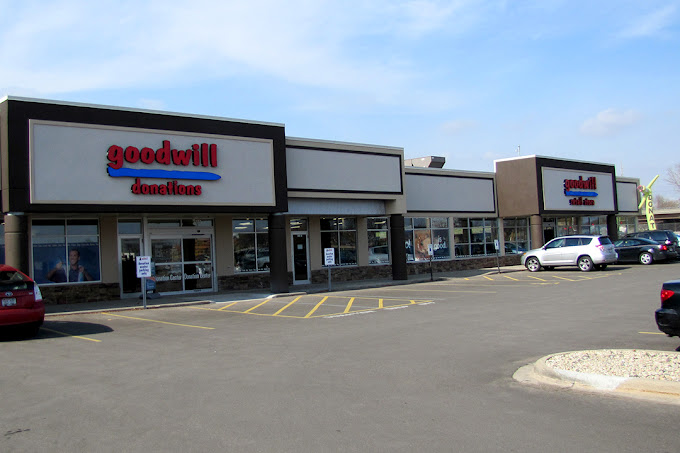 Exterior of a Goodwill store with an adjacent donation center, featuring a parking lot with several parked cars on a clear day.