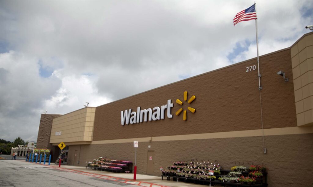 Exterior view of a Walmart store with an American flag flying on a pole outside. The store's logo is prominently displayed on the building.