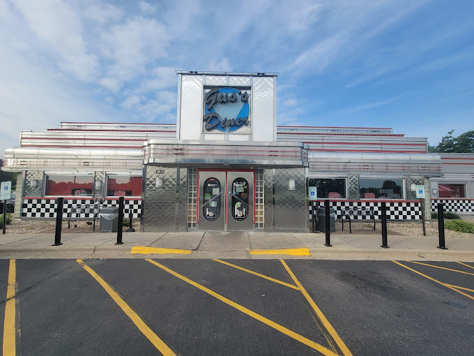 Front exterior of a diner with a sign reading "Jax's Diner." The building has a retro style with chrome accents, checkerboard trim, large windows, and double glass doors beneath a prominent sign.