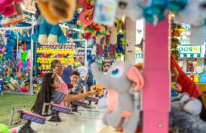 People playing a carnival game surrounded by various colorful stuffed animals at a fairground.