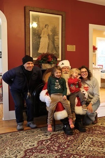 A family poses with Santa Claus in a room with red walls and a patterned carpet.