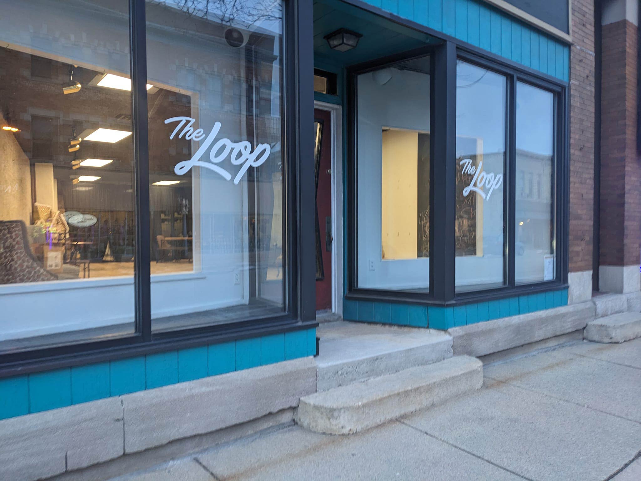 A storefront with large windows displays the name "The Loop". The windows are framed with black trim and the building exterior is blue. The entrance features a recessed door with steps leading up.