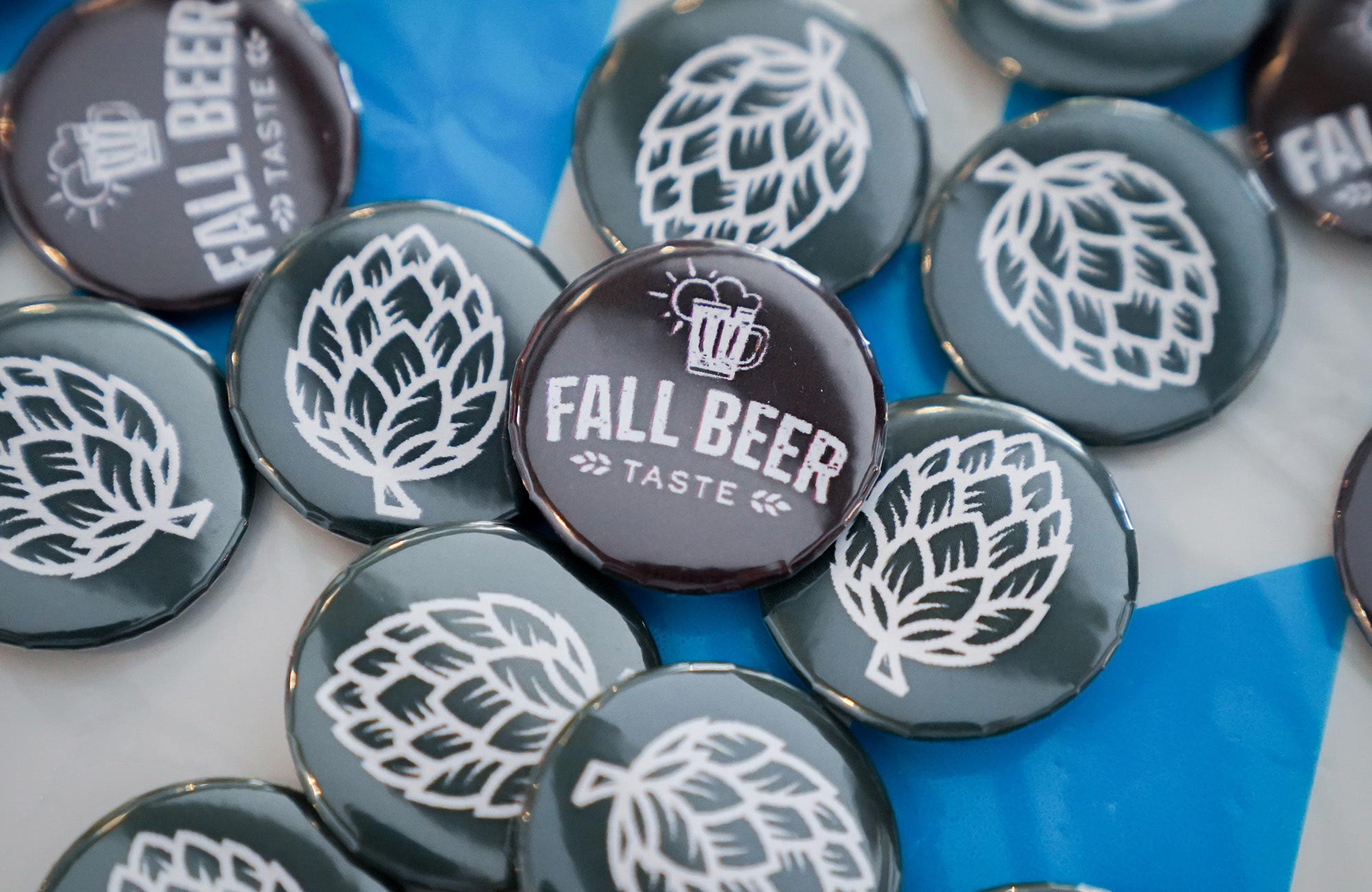 Round badges featuring a "Fall Beer Taste" design and hop illustrations are displayed on a table.