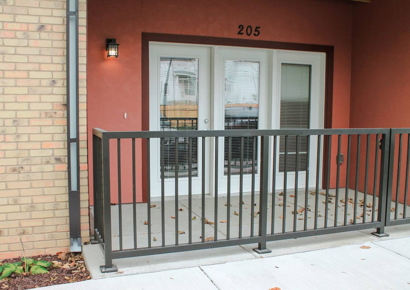 A ground-floor balcony with metal railing outside a building, featuring double glass doors, marked with the number 205.