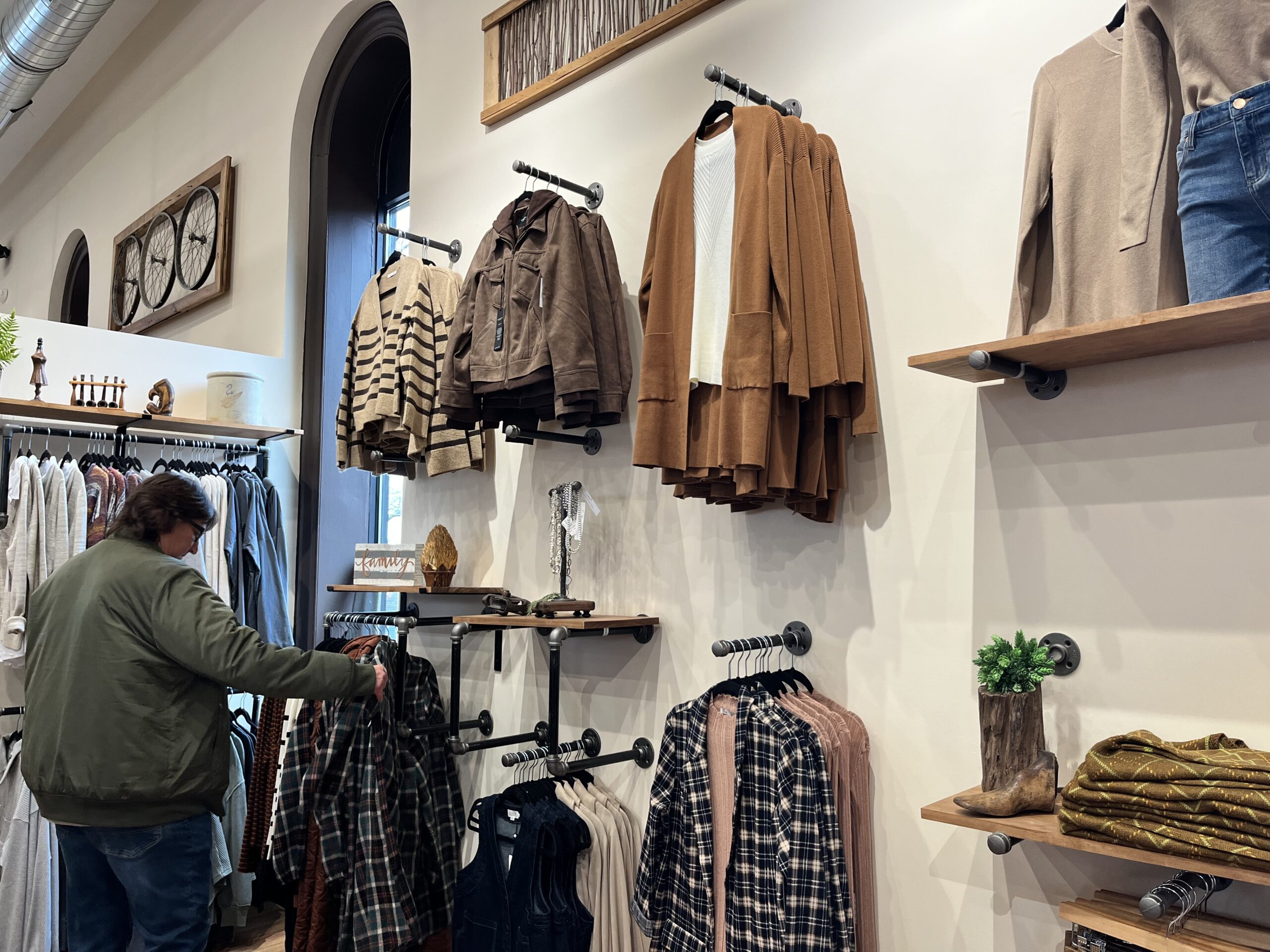 A person browses clothing in a store, with jackets, shirts, and sweaters displayed on the walls and shelves.