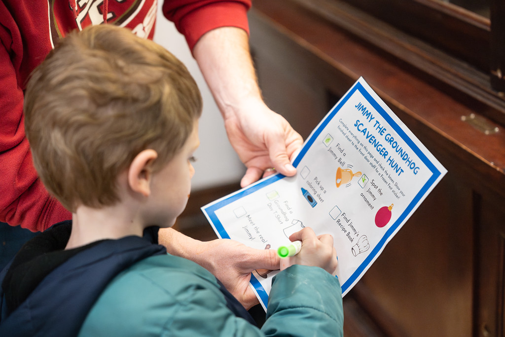 A child marks off items on a scavenger hunt sheet titled "Jimmy the Groundhog" with the help of an adult.