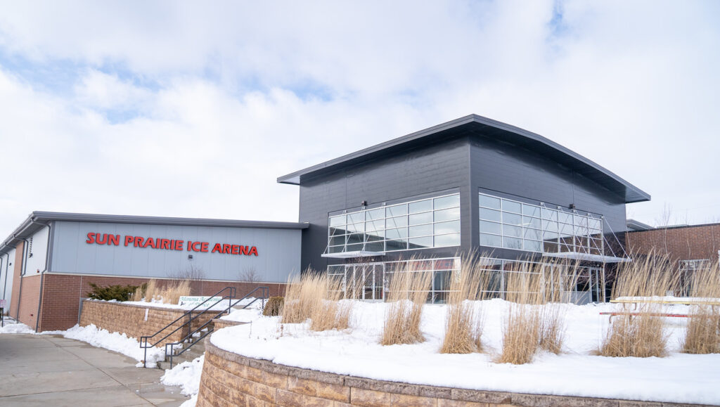 Exterior of Sun Prairie Ice Arena on a snowy day, featuring modern architecture with large windows and a sign on the building.