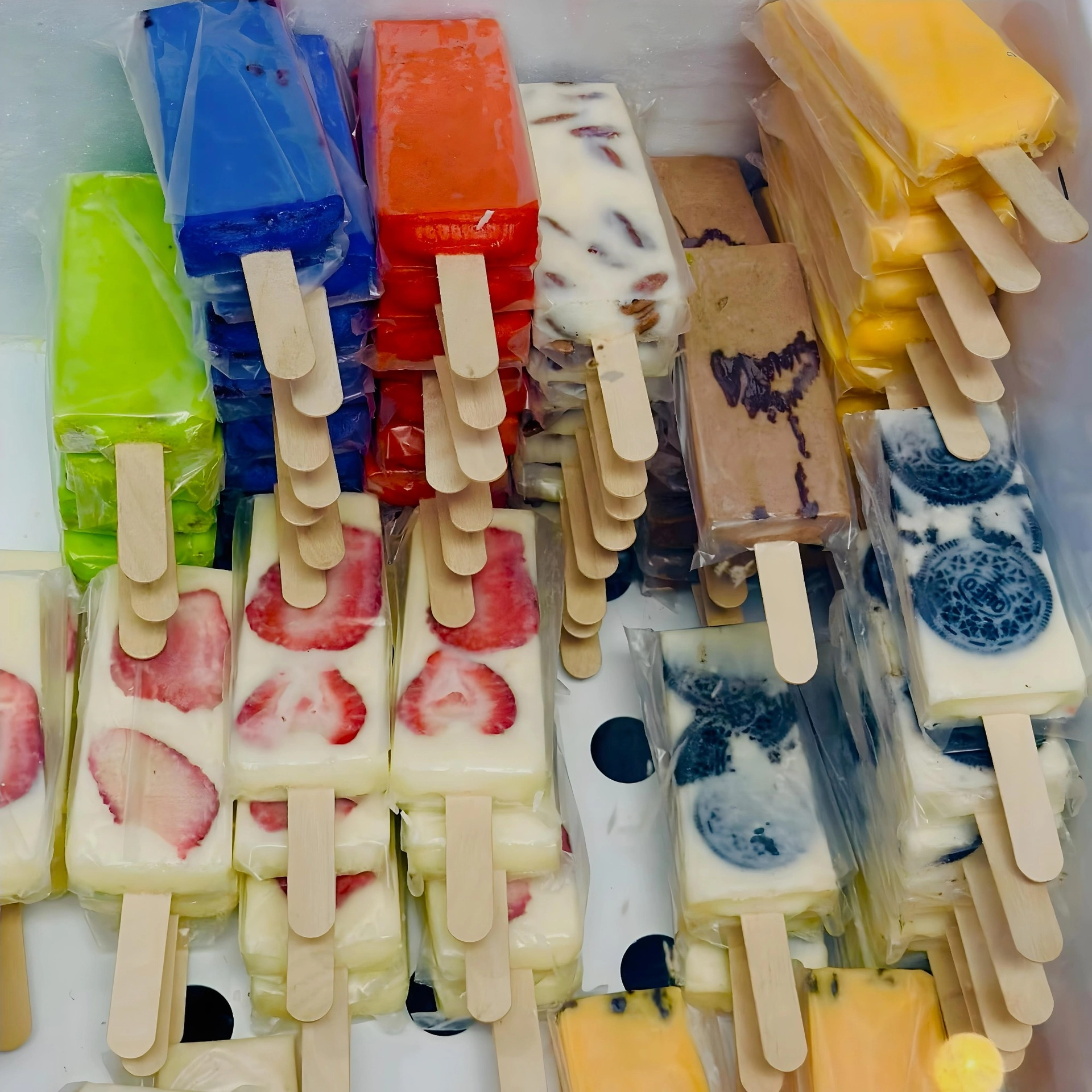 Assorted colorful popsicles, including fruit and cream varieties, neatly stacked in rows inside a freezer.