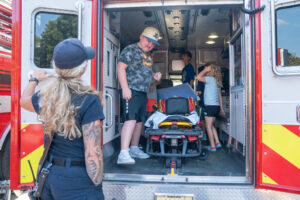 Several children explore the inside of an ambulance while an emergency responder stands nearby, observing them.
