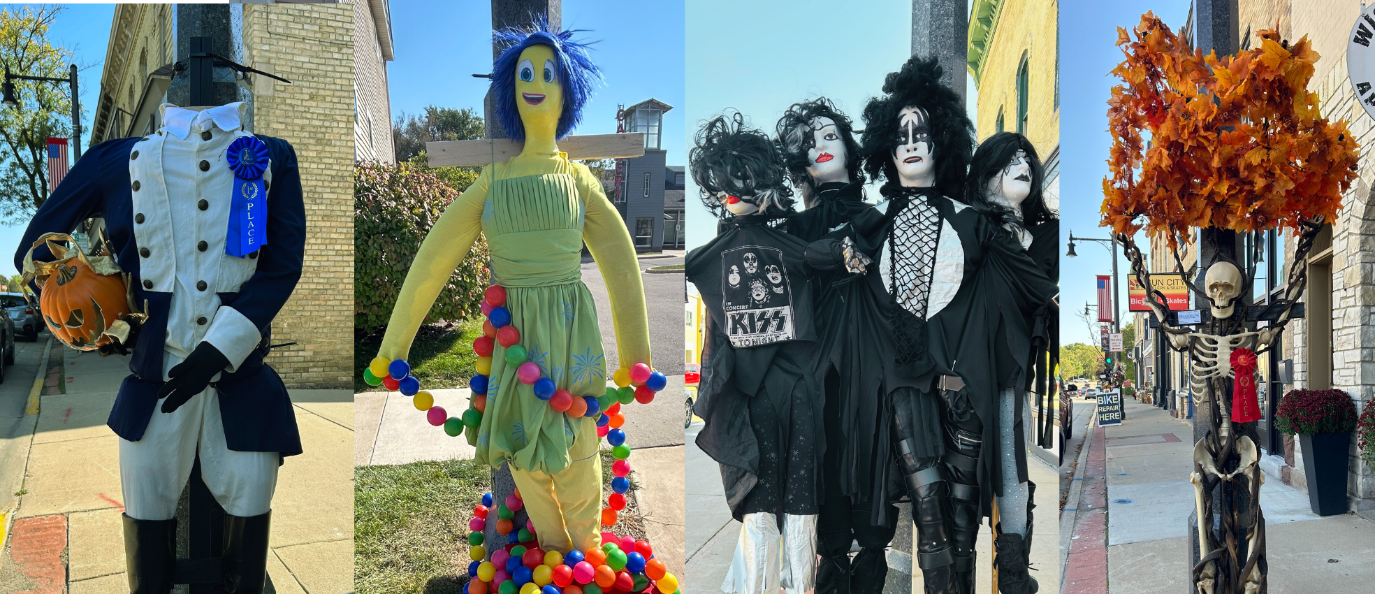 Four scarecrows stand on a sidewalk: a colonial soldier with a blue ribbon, a yellow figure in a green dress, three figures dressed as KISS band members, and a skeleton holding orange leaves.