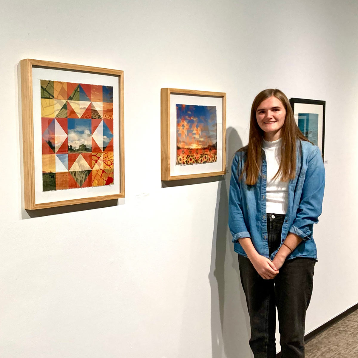 A young woman stands next to framed artworks displayed on a white gallery wall.