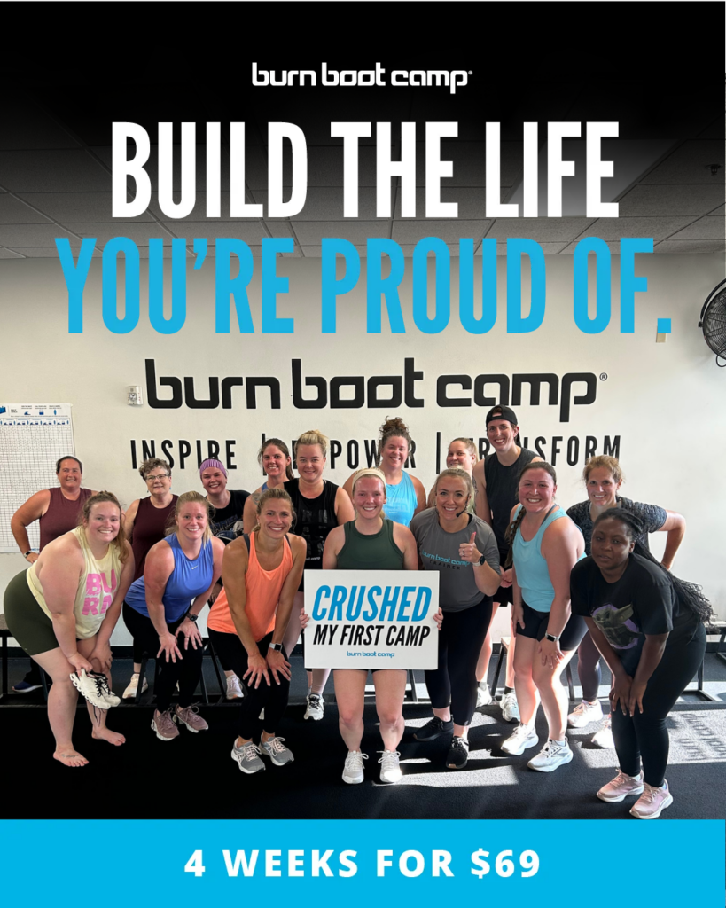 A group of people pose and smile in a gym, holding a sign that reads “Crushed My First Camp.” A banner advertises “4 Weeks for $69” at Burn Boot Camp.