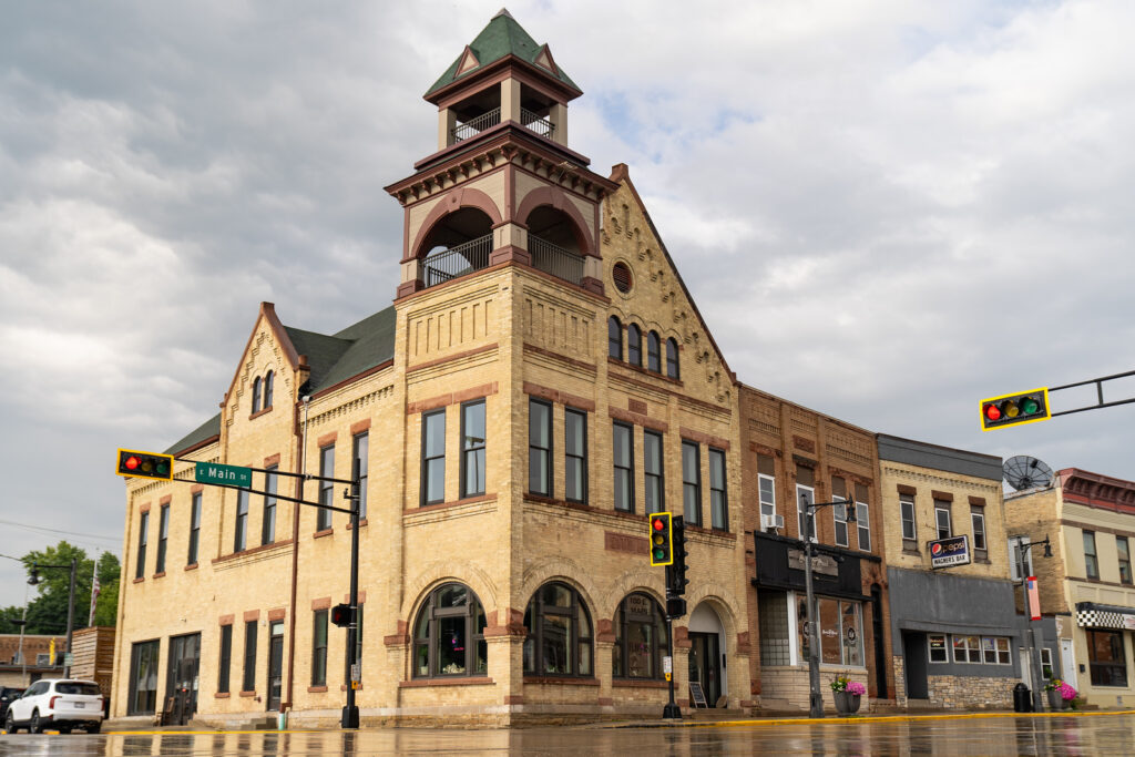 A three-story yellow brick corner building with a prominent bell tower under a cloudy sky.