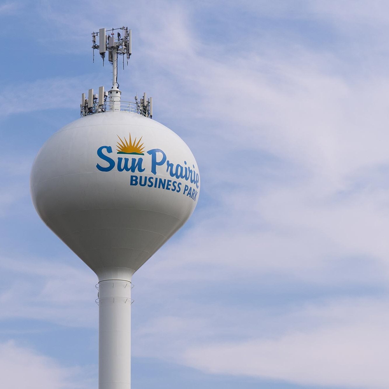 Water tower labeled "Sun Prairie Business Park" with antennas on top, set against a partly cloudy sky.