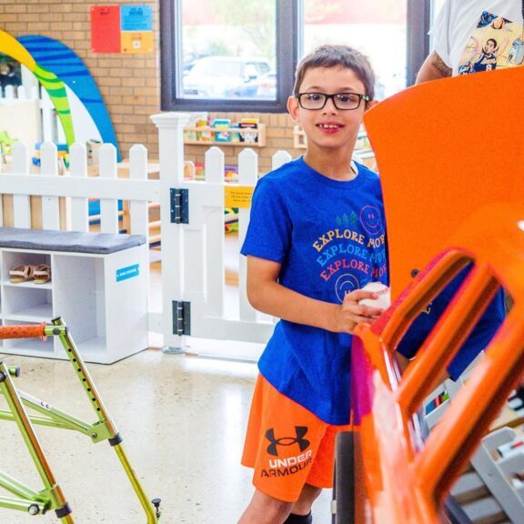 A young boy interacts with a colorful exhibit at an indoor play area, featuring a large orange structure and a green climbing frame.