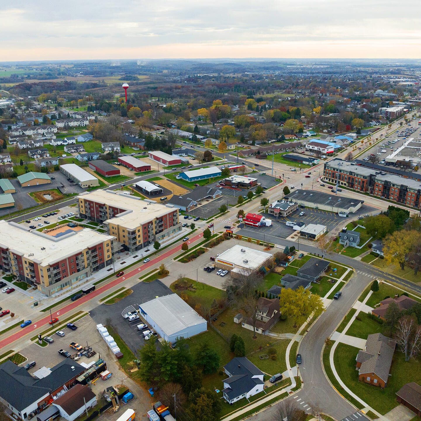 Aerial view of a suburban area with residential buildings, commercial areas, streets, and green spaces on a cloudy day.