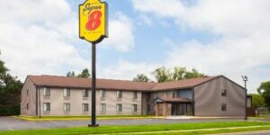 A two-story grey building with a yellow and red sign reading "Super 8 by Wyndham" near a parking lot and bordered by grass.