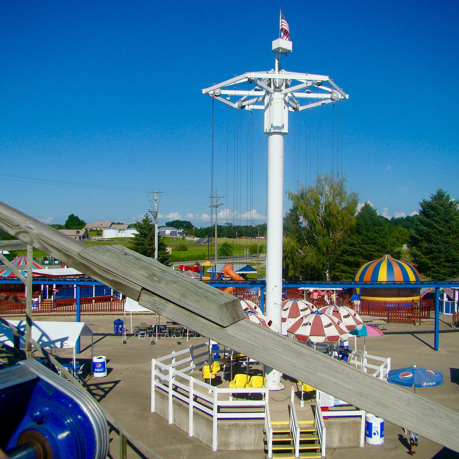 Amusement park with a tall swing ride in the center, various vibrant rides and attractions around, benches, and an overcast sky.