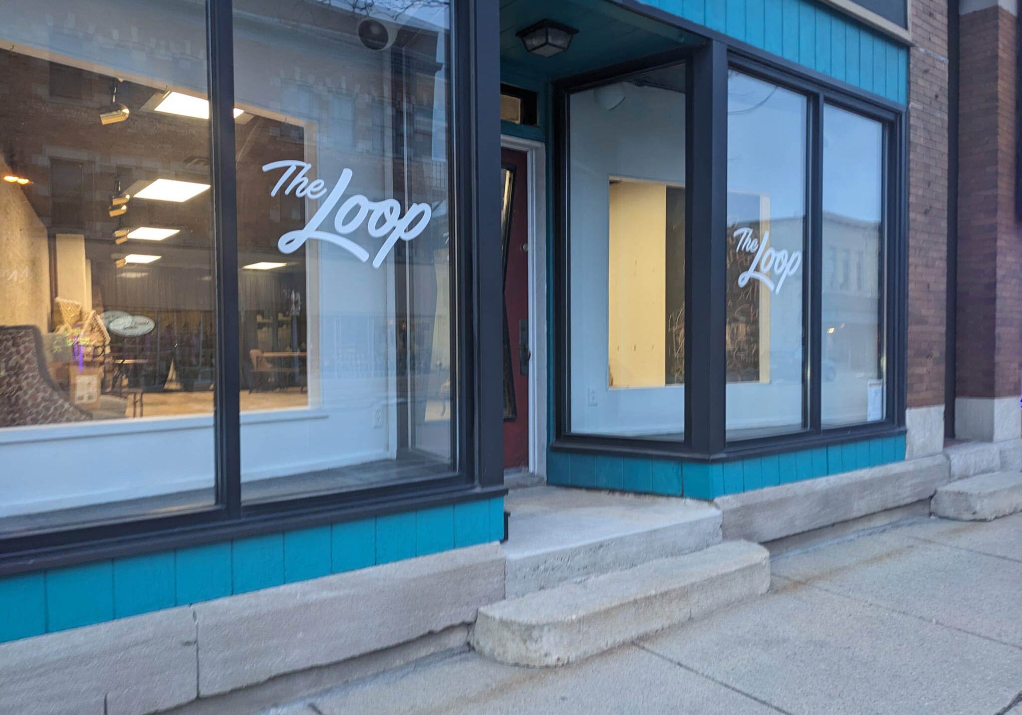 A storefront with large windows displays the name "The Loop". The windows are framed with black trim and the building exterior is blue. The entrance features a recessed door with steps leading up.