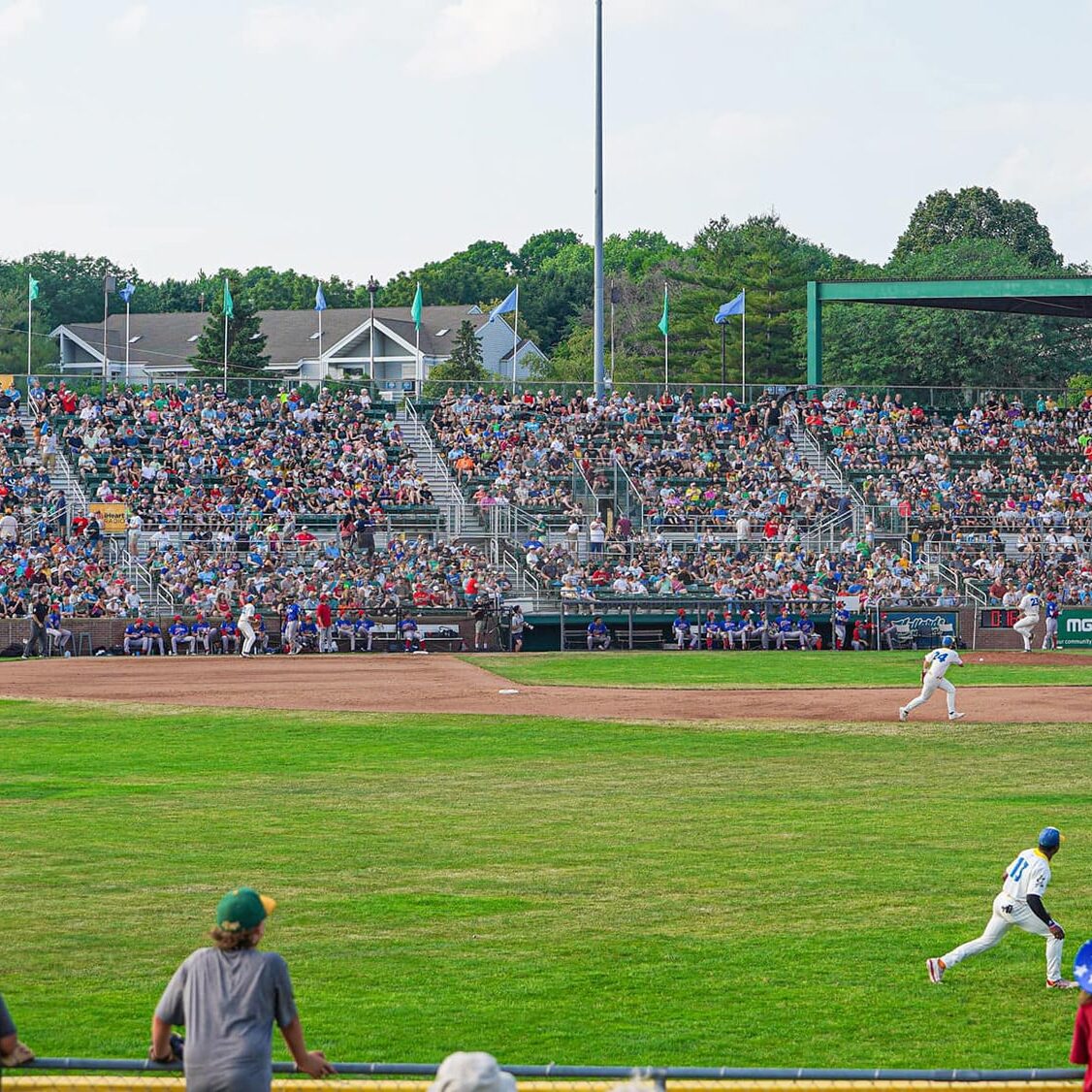 A baseball game in progress at a stadium with a large crowd in the stands. Players are seen on the field, and spectators watch from the stands and behind a fence.